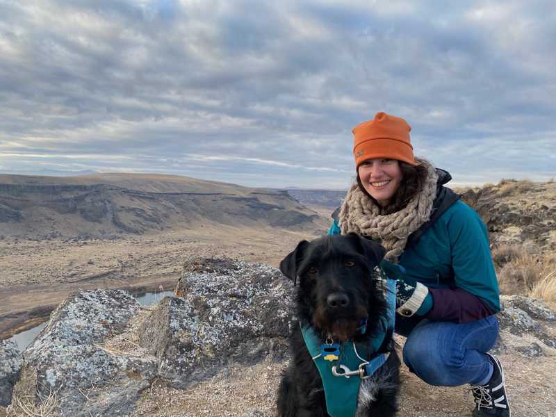 Dog wearing Front Range Dog Harness next to a woman with mountains in the background